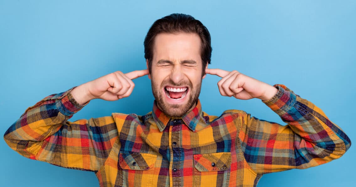 Man is holding his ears in response to his hvac making loud noise.