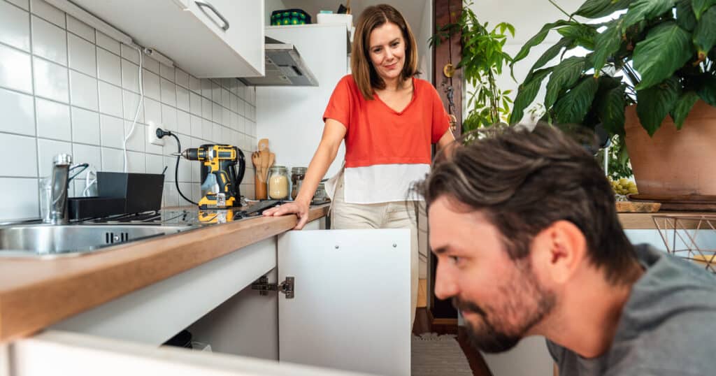 A homeowner smiles as he looks under the sink because he just purchased the best garbage disposal for the money.
