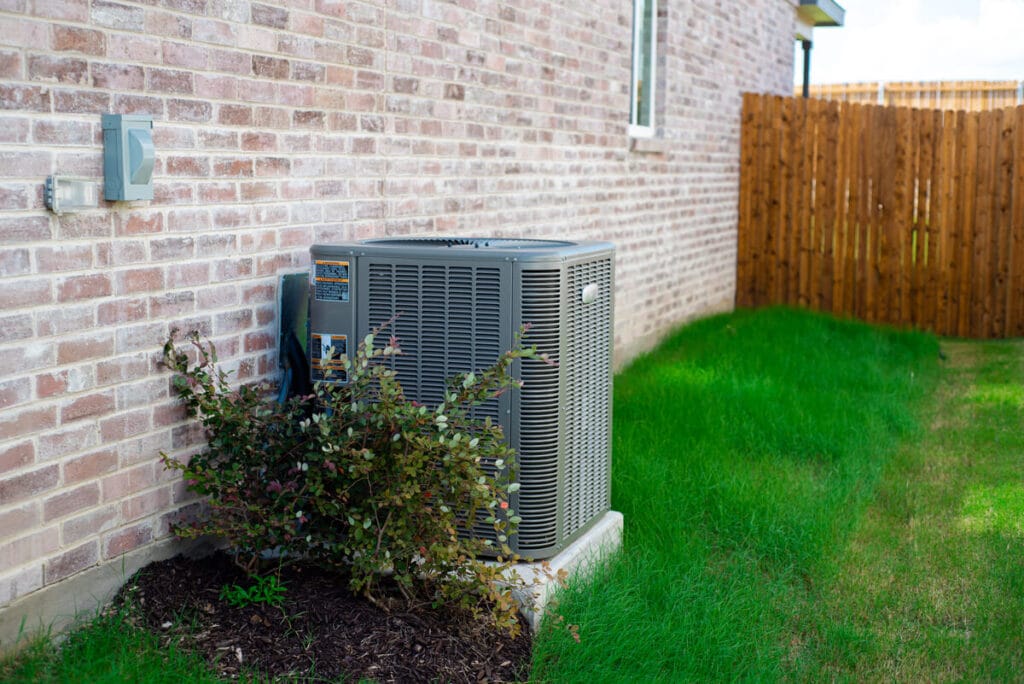 An HVAC unit in a beautiful yard is a reminder that spring HVAC maintenance is important.